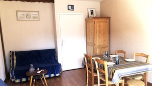 A dining area with a wooden table set for four, surrounded by wooden chairs. A blue sofa is positioned against the wall, and a wooden cabinet is visible in the corner. - Ty-Bi - Studio in location vacances in Carnac, Légenèse / Ty-Bihan - UD220 (Carnac)
