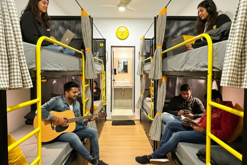 A dormitory room with bunk beds, a clock on the wall, and a door leading to a bathroom.