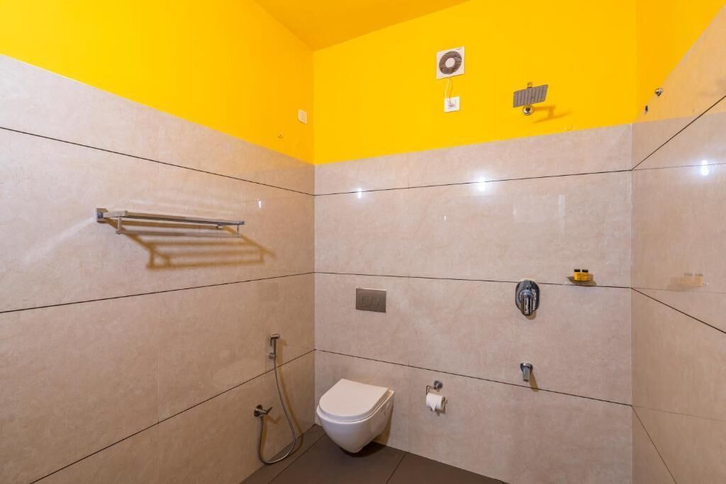 A small, bright bathroom with a yellow ceiling, a white toilet, a towel rack, and a shower.