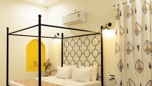 Ein Bett mit Baldachin, dessen Kopfteil mit kreisförmigen Mustern verziert ist, ein Deckenventilator, eine Klimaanlage, ein Nachttisch und ein Sessel.