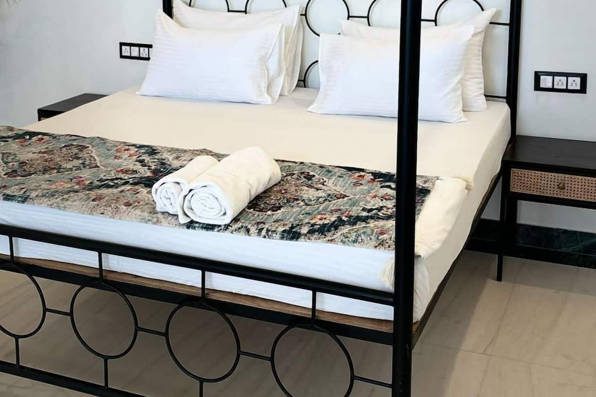 Una cama con dosel, cabecero geométrico, ropa de cama blanca y una manta estampada.