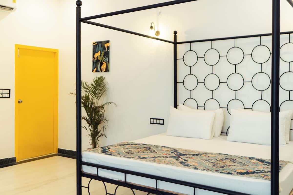 Una cama con dosel y un cabecero geométrico, un ventilador de techo y una puerta amarilla.