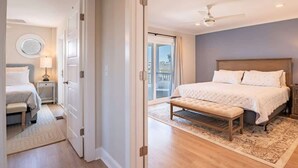 Een slaapkamer met een groot bed, een bankje, een nachtkastje, een plafondventilator en uitzicht op het balkon.