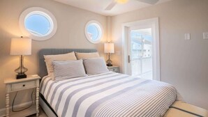 Ein Schlafzimmer mit einem Bett, zwei Nachttischlampen, einem Deckenventilator und zwei Fenstern.