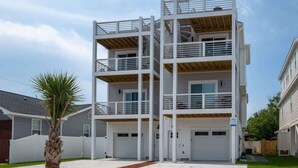 A multi-story residential building with a white exterior, multiple balconies, and a garage. - Lone Star Breeze (Carolina Beach)