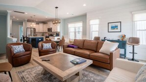 A modern living room with a brown leather sofa, a wooden coffee table, and a dining area with a blue table. - Lone Star Breeze (Carolina Beach)