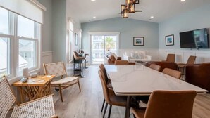 A spacious room with a large dining table, comfortable seating, a television, and large windows. - Lone Star Breeze (Carolina Beach)