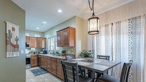 A kitchen with wooden cabinets, a dining table with chairs, and a hanging light fixture. - Luxe Top-Floor Condo|Camelback Views| Heated Pool (Scottsdale)