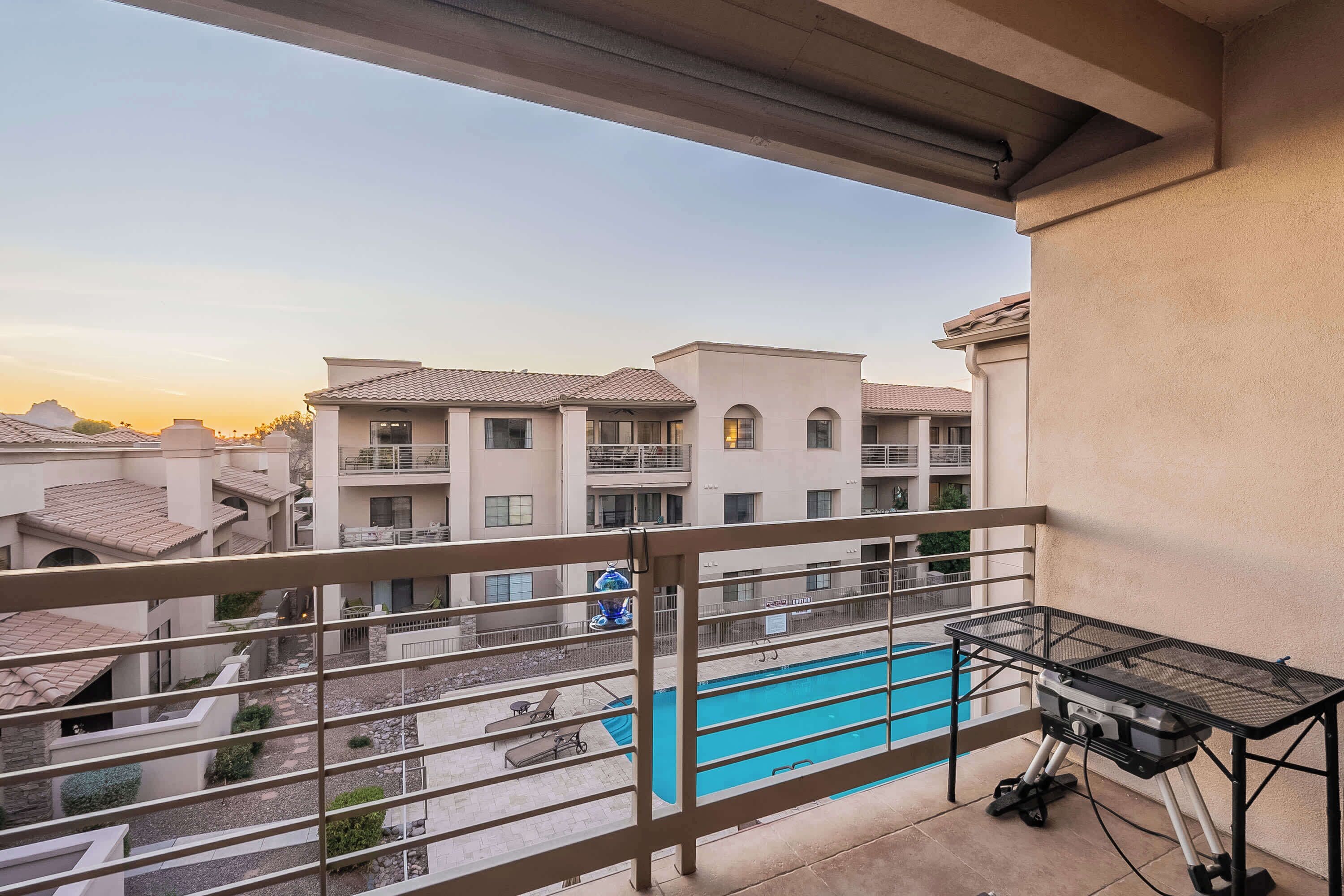 A balcony with a pool, a grill, and a view of neighboring buildings.
