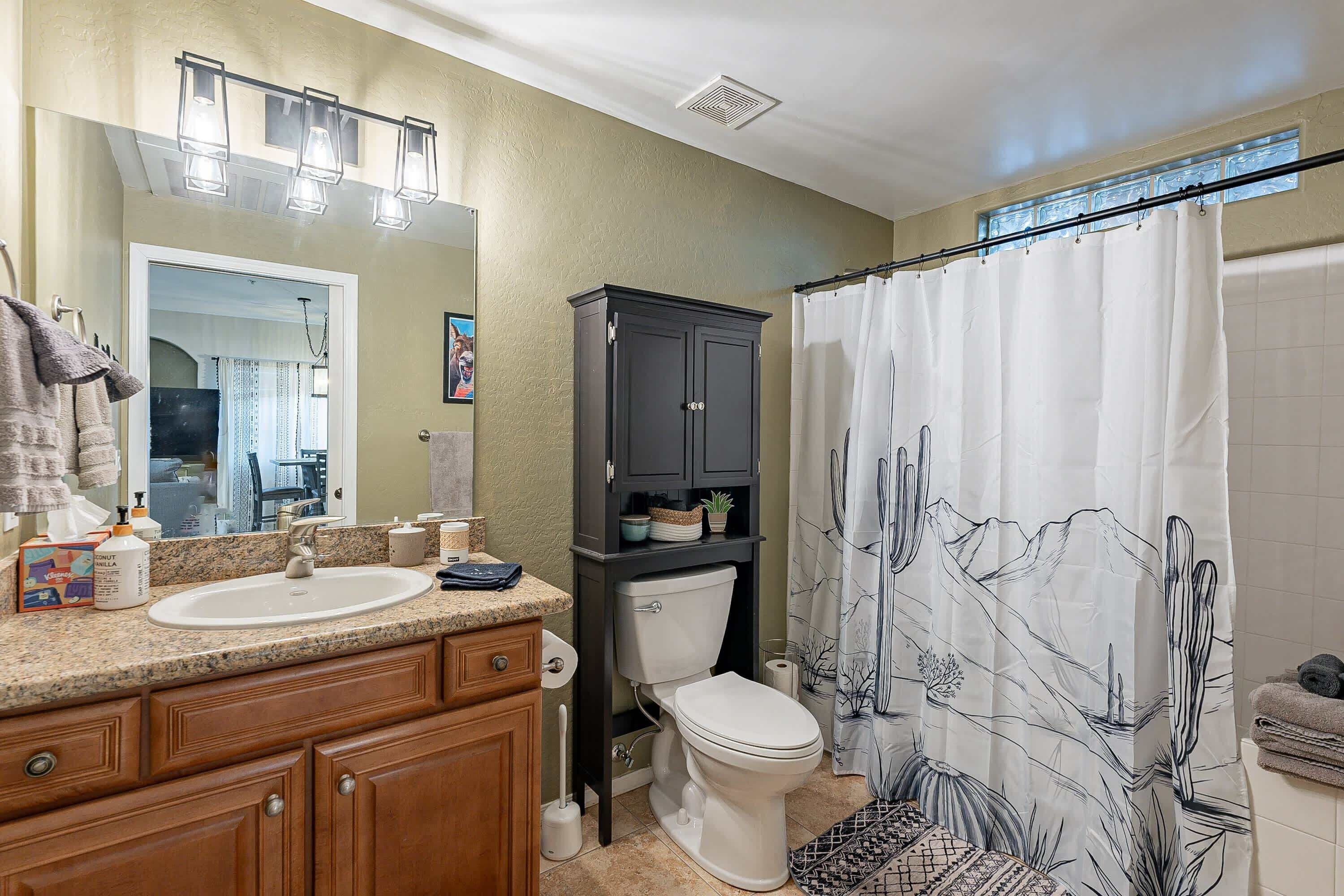 A bathroom with a double sink, vanity, dark cabinet, toilet, shower curtain, and a mirror.