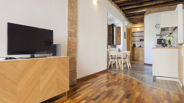 A modern kitchen with a built-in oven, a dining area with a table and chairs, and a TV on a wooden cabinet. - Giardini 47 - Morada (Cagliari)