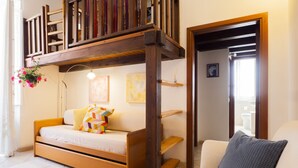 Une chambre avec un lit superposé en bois, un canapé-lit, une plante suspendue et un tableau au mur.