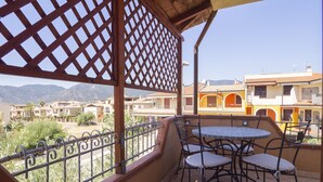 Un balcón con una mesa y sillas, con vistas a una zona residencial con edificios coloridos y montañas al fondo.