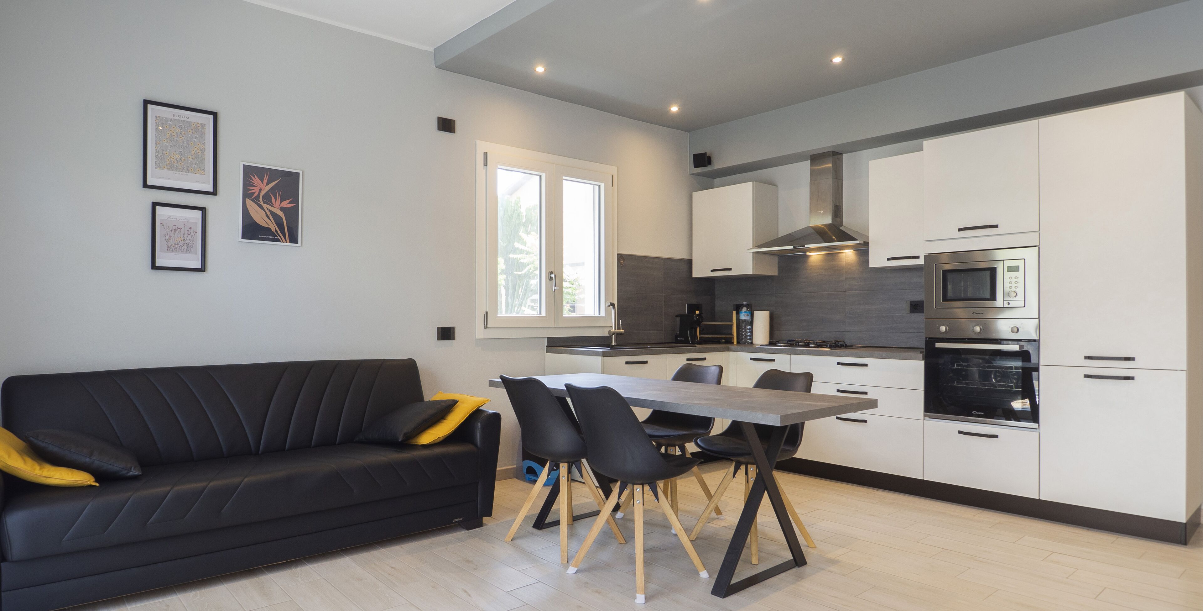 Una cucina moderna con mobili bianchi, un piano di lavoro nero e un'area pranzo con tavolo e sedie neri.