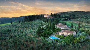 A villa with a swimming pool surrounded by olive groves and cypress trees, set against a backdrop of rolling hills and a sunset sky. - Il Casolese Vignamaggio Private Pool  (Greve in Chianti)