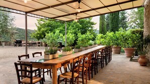 An outdoor patio with a long wooden table and chairs, surrounded by potted plants and a view of the landscape. - Il Casolese Vignamaggio Private Pool  (Greve in Chianti)