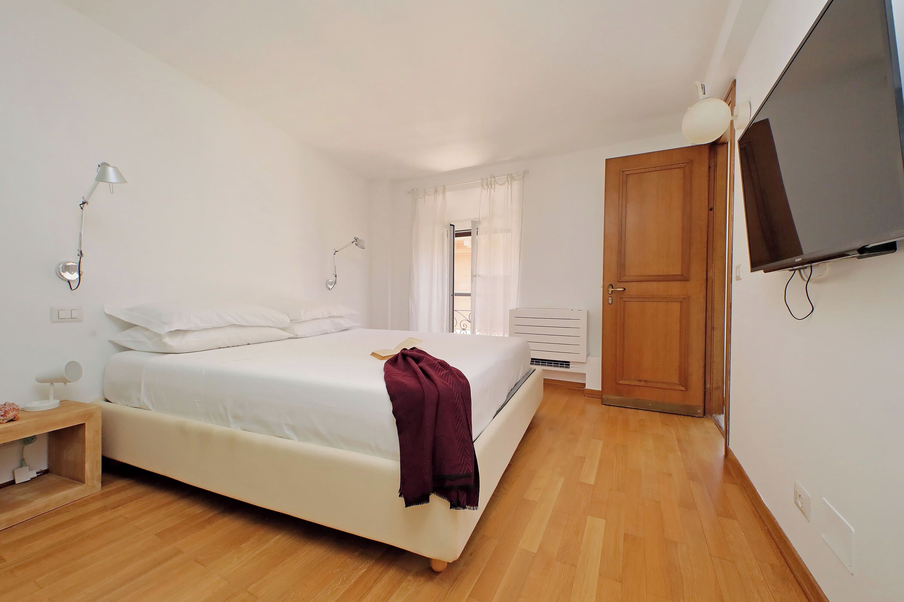 Een slaapkamer met een bed, nachtkastje, lamp, televisie en een houten deur.