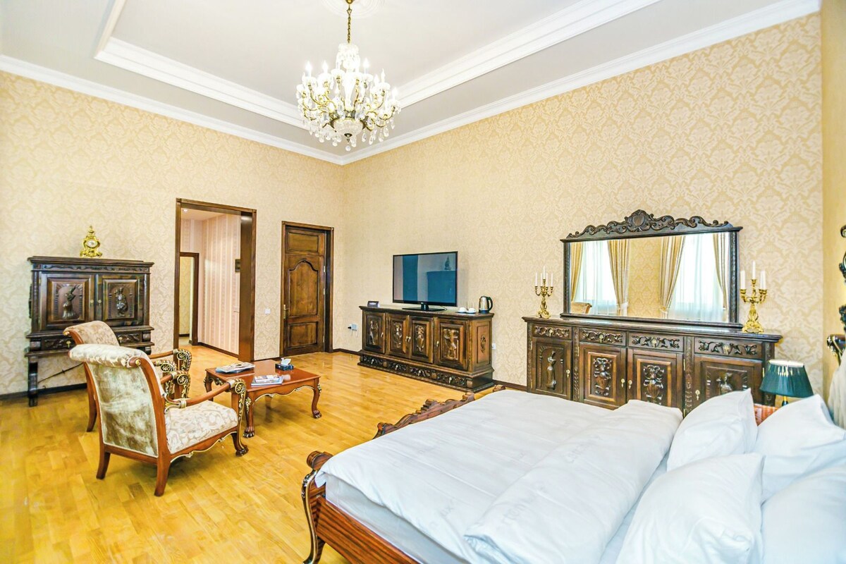 A hotel room with a large bed, a television, a wooden dresser, a chair, and a chandelier.