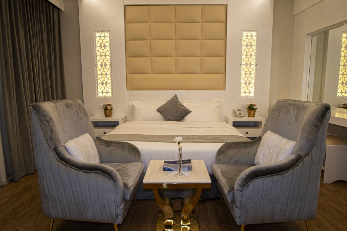 A hotel room with a large bed, two armchairs, a small table, and decorative lighting.