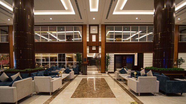 A spacious lobby with a central marble floor, flanked by rows of sofas and armchairs, large wooden columns, and a modern reception desk. - towers hotel (Buraydah)