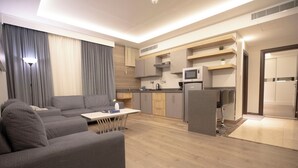 Ein modernes Wohnzimmer mit grauem Sofa, einem kleinen Tisch und einer Küchenzeile mit Mikrowelle und Schränken.