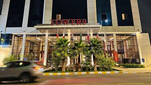 A hotel with a modern facade, large windows, and a prominent entrance with palm trees. - towers hotel (Buraydah)