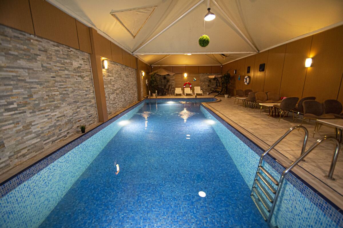 An indoor swimming pool with clear blue water, surrounded by lounge chairs and a stone wall.