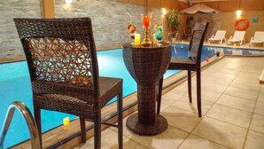 A poolside area with wicker chairs and a table with candles and drinks. - towers hotel (Buraydah)