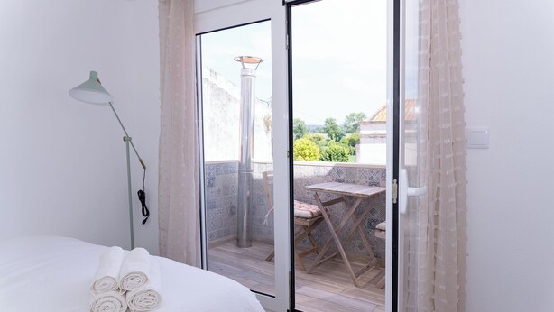 Une chambre d’hôtel avec un lit, une lampe et une porte-fenêtre coulissante donnant sur un espace extérieur équipé d’une table et de chaises.