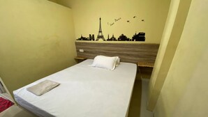Een enkel bed met een witte matras en een beige deken, een houten hoofdbord en een muurdecoratie met bezienswaardigheden van Parijs.