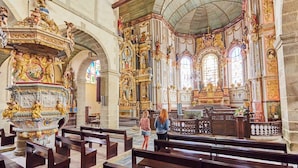 Interior de iglesia ornamentado, con techos altos, detalles de madera labrada y un altar central.