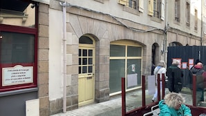 Un edificio con una puerta amarilla, un letrero con texto y una persona sentada a una mesa con una pizza.