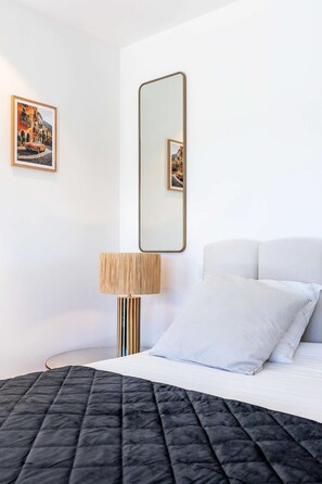A neatly arranged hotel room with a bed, a bedside lamp, a large mirror, and two framed pictures on the wall. - Suite "La Capri" - Heated pool & SPA (Plaissan)