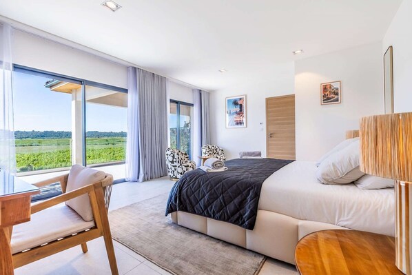 A modern bedroom with a large bed, a seating area with a view, and a balcony with curtains. - Suite "La Capri" - Heated pool & SPA (Plaissan)