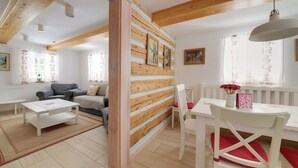 A living room with a wooden wall, a white dining table with chairs, and a sofa. - Dom Nad Wodospadem pod Snieznymi Kotlami (Jelenia Góra)