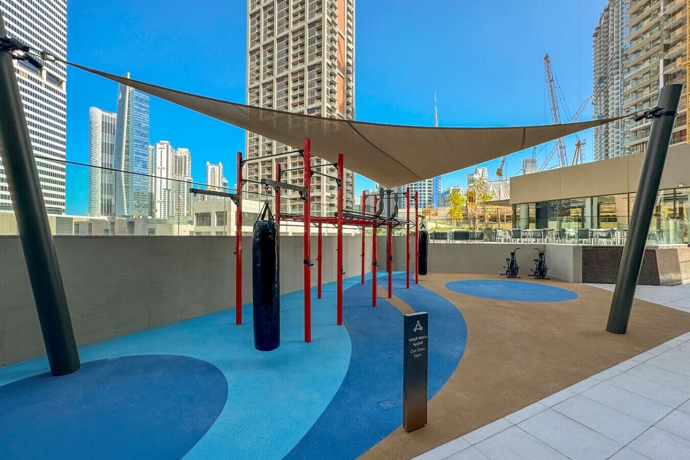 An outdoor gym with exercise equipment, a blue padded floor, and a canopy.
