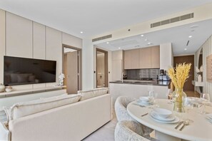 A modern kitchen with a central island, a dining area with a round table set for four, and a living area with a sofa and a TV.