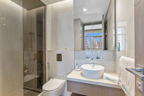 Uma casa de banho moderna com cabine de duche em vidro, lavatório branco e um espelho grande que reflete a vista da cidade.