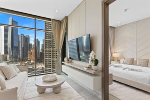 Quarto de hotel moderno com uma janela grande que oferece vista para a cidade, televisão de tela plana, sofá e mesa de jantar.