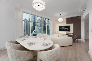 A modern living room with a dining area, large windows, a flat-screen TV, and a city view.