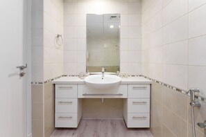 A modern bathroom with a white sink, two drawers, a mirror, and a shower.