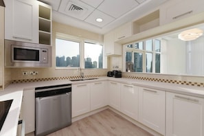A modern kitchen with white cabinets, a built-in microwave, a dishwasher, and a window with a city view.