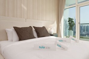 A hotel room with a large bed, two pillows, a nightstand with a lamp, and a view of a cityscape through a large window. - Exquisite 2-Bedroom with Panoramic Marina view (Dubai)