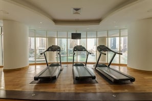 A gym with three treadmills, large windows, and a view of a cityscape.