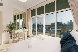 A modern hotel room with a large bed, a desk, and a view of the city skyline through floor-to-ceiling windows. - Exquisite 2-Bedroom with Panoramic Marina view (Dubai)