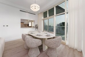 A modern dining room with a round table, white chairs, and a city view through large windows. - Exquisite 2-Bedroom with Panoramic Marina view (Dubai)