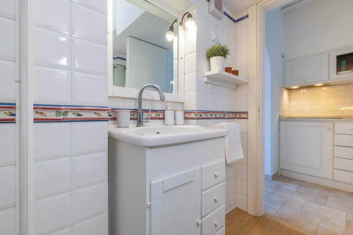 Une salle de bain moderne avec un lavabo blanc, un miroir et un meuble. Une petite plante est posée sur une étagère au-dessus du lavabo, et une serviette est accrochée à la porte du meuble.