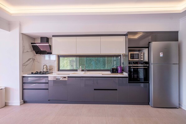 A modern kitchen with grey cabinets, a stainless steel refrigerator, a built-in oven, and a microwave.
