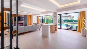 Amplia sala de estar con sofá, televisión y chimenea. Hay una mesa de comedor con sillas y vistas a una piscina exterior.