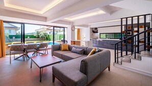 Amplia sala de estar con sofá, mesa de comedor y sillas, una cocina al fondo y una escalera.
